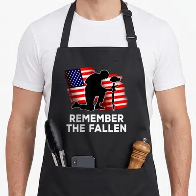 Patriotic remember american flag apron - Kneeling soldier silhouette on distressed flag with text REMEMBER THE FALLEN — shown on a black cotton canvas apron against a white background