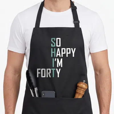 Bday 40th birthday apron - SO HAPPY I'M FORTY text in white and light blue stacked typography — shown on a black cotton canvas apron against a white background