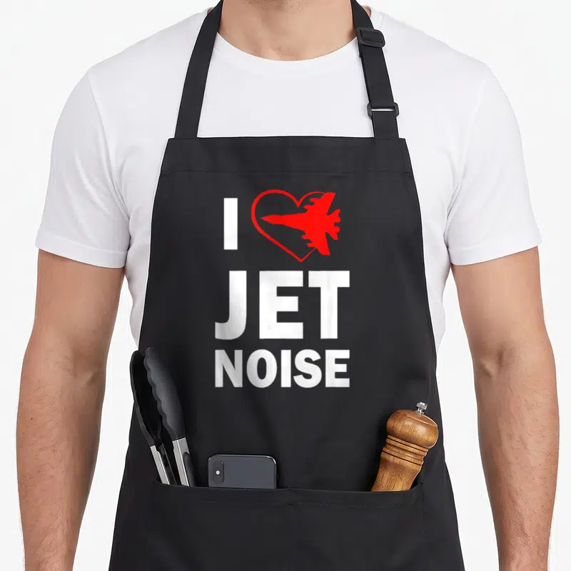 Jet air show apron - White I and stacked JET NOISE text beside red heart containing jet plane silhouette — shown on a black cotton canvas apron against a white background