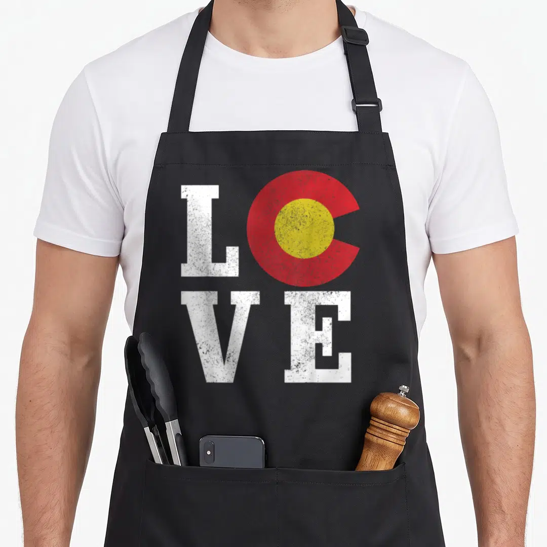 Colorado flag pride apron - Distressed white letters L V E and red yellow circle arranged in a square grid pattern — shown on a black cotton canvas apron against a white background