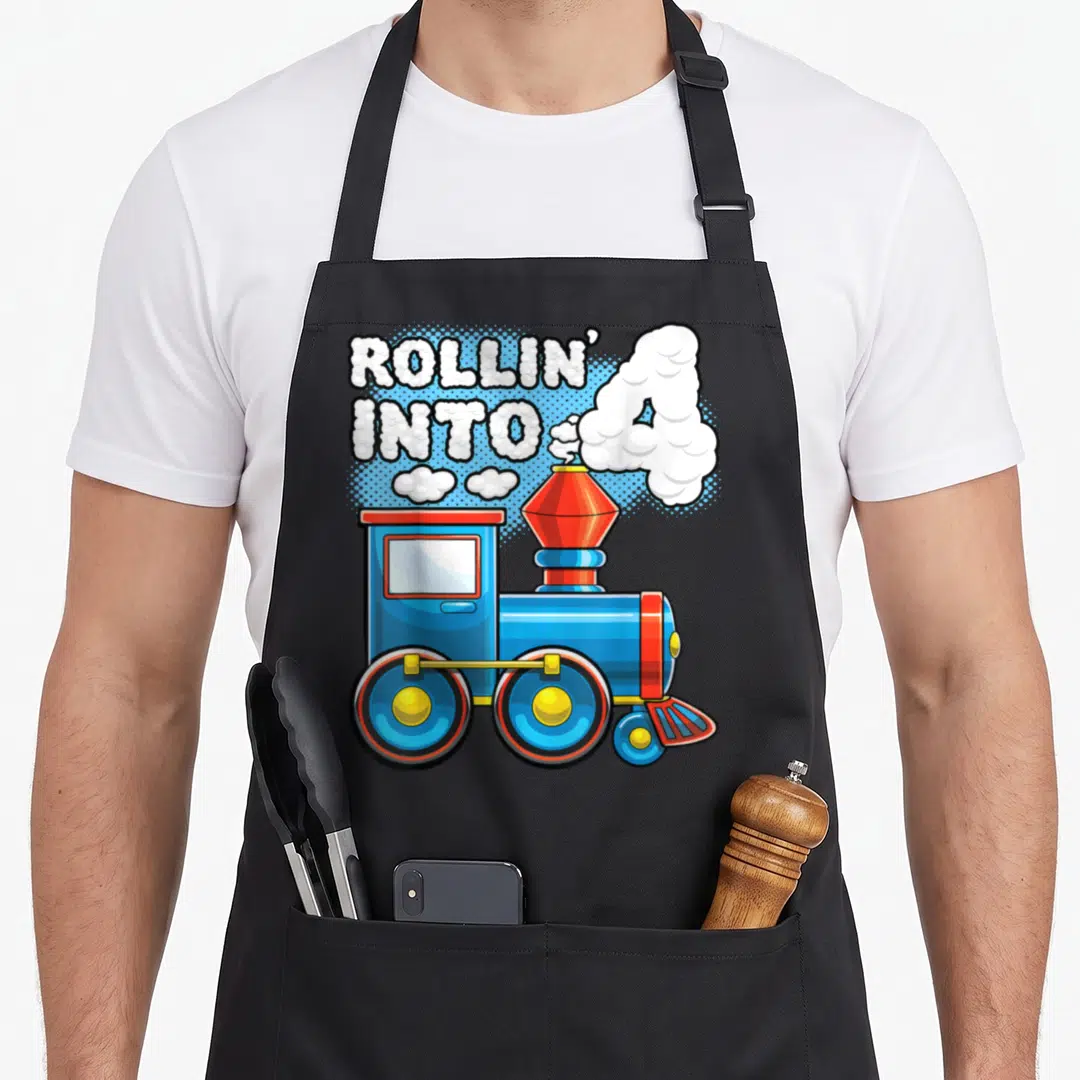 Supply birthday apron - Blue cartoon train with white smoke forming the number 4 and text Rollin Into 4 — shown on a black cotton canvas apron against a white background