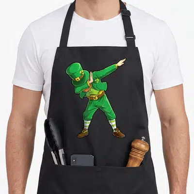 Leprechaun dab st patrick day aprons - Cartoon leprechaun dabbing in green and yellow with brown shoes and striped socks — shown on a black cotton canvas apron against a white background