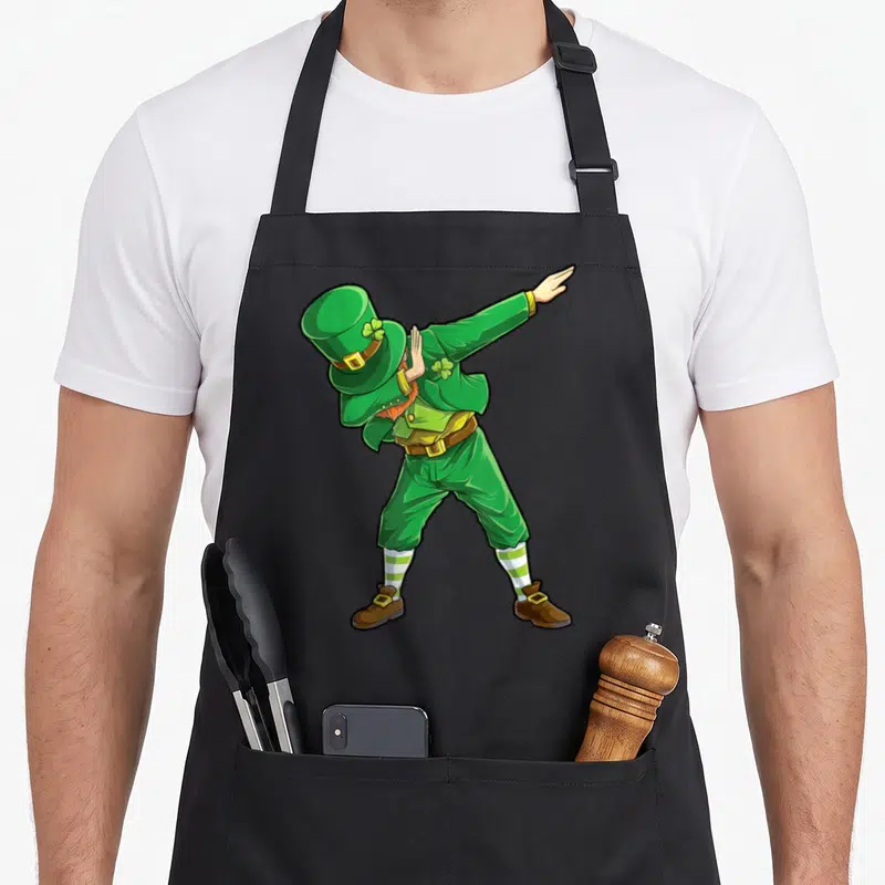 Leprechaun dab st patrick day aprons - Cartoon leprechaun dabbing in green and yellow with brown shoes and striped socks — shown on a black cotton canvas apron against a white background