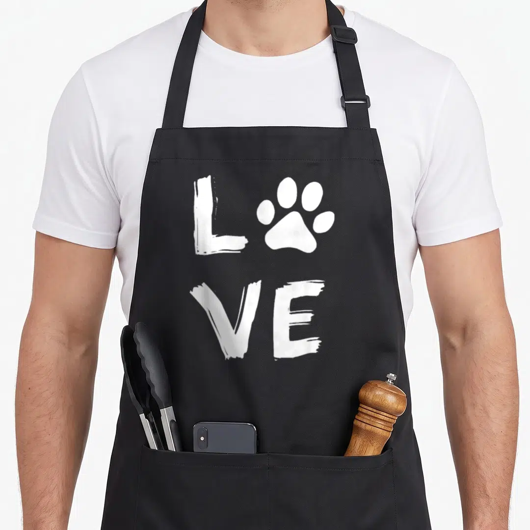 Owner paw print apron - White brush stroke text reading LOVE with a paw print replacing the O on black fabric — shown on a black cotton canvas apron against a white background