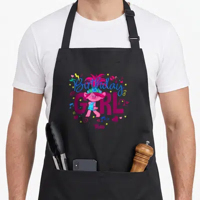 Sassy birthday apron - Poppy Troll character with Birthday GIRL text and scattered hearts notes stars in magenta blue — shown on a black cotton canvas apron against a white background