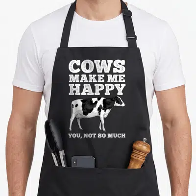 Dairy farmers apron - Cows Make Me Happy You Not So Much text above realistic black and white cow illustration — shown on a black cotton canvas apron against a white background