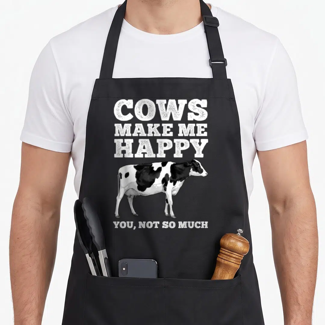 Dairy farmers apron - Cows Make Me Happy You Not So Much text above realistic black and white cow illustration — shown on a black cotton canvas apron against a white background