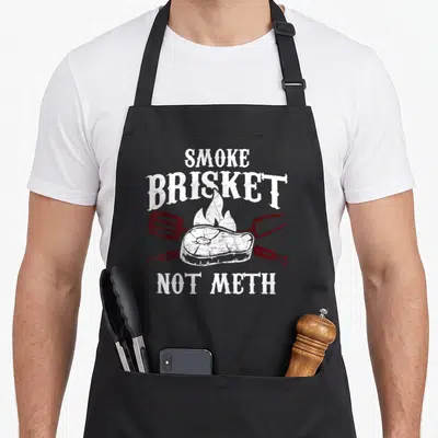 Meth meat aprons - White Smoke Brisket Not Meth text over brisket on fire with crossed red spatula and fork — shown on a black cotton canvas apron against a white background