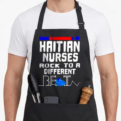 Haitian nurse apron - Distressed white text reading Haitian Nurses Rock to a Different Beat with blue anatomical heart — shown on a black cotton canvas apron against a white background