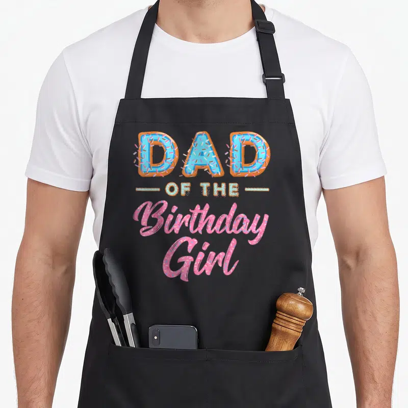 Bday donut apron - Stacked text DAD OF THE Birthday Girl in blue and pink donut lettering — shown on a black cotton canvas apron against a white background