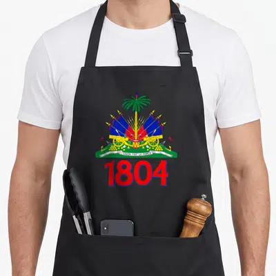 Flag haitian boy apron - Coat of arms with palm tree, cannons, flags, ribbon text, and large red 1804 numbers — shown on a black cotton canvas apron against a white background