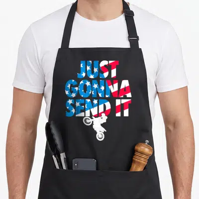 Send american flag apron - Just Gonna Send It text with jumping motocross rider in red white blue stars and stripes — shown on a black cotton canvas apron against a white background