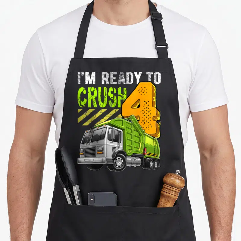 Garbage 4th birthday truck apron - I'M READY TO CRUSH 4 text above lime green cartoon garbage truck with orange number — shown on a black cotton canvas apron against a white background