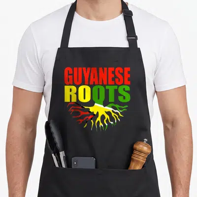 Storecastle pride apron - GUYANESE ROOTS text with red yellow and green flag-filled roots — shown on a black cotton canvas apron against a white background