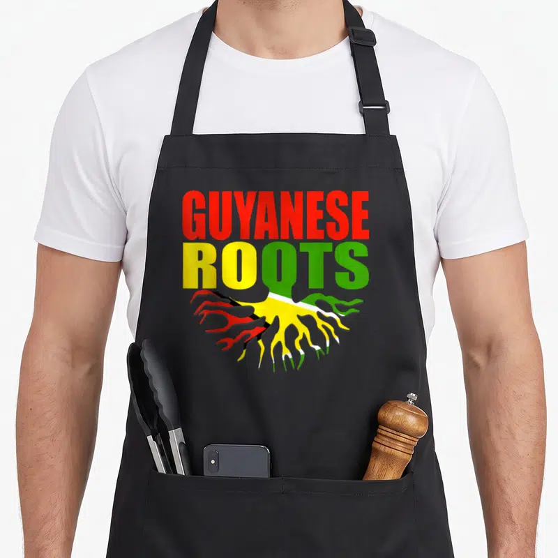 Storecastle pride apron - GUYANESE ROOTS text with red yellow and green flag-filled roots — shown on a black cotton canvas apron against a white background
