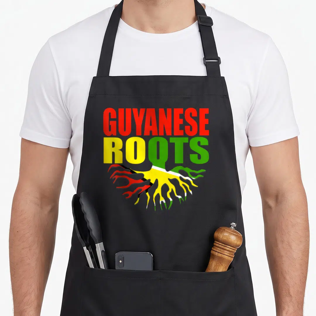 Storecastle pride apron - GUYANESE ROOTS text with red yellow and green flag-filled roots — shown on a black cotton canvas apron against a white background