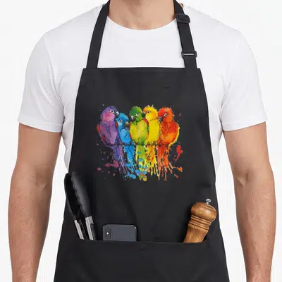 Colourful parrot bird apron - Five colorful parrots perched on a black line with watercolor splatters in purple, blue — shown on a black cotton canvas apron against a white background