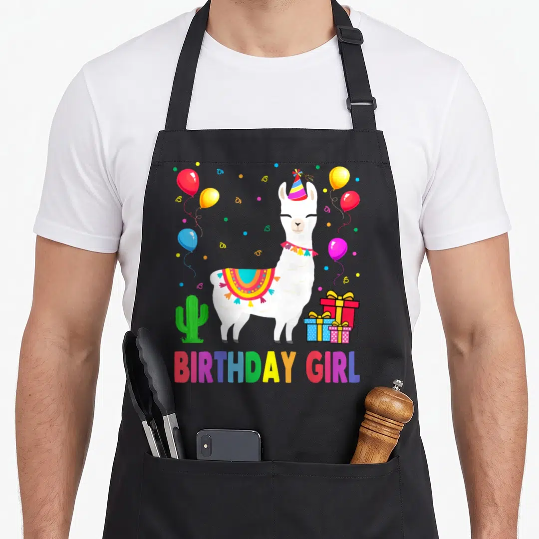 Cactus alpaca apron - White llama wearing party hat and saddle, surrounded by balloons, cactus, gifts, and BIRTHDAY — shown on a black cotton canvas apron against a white background