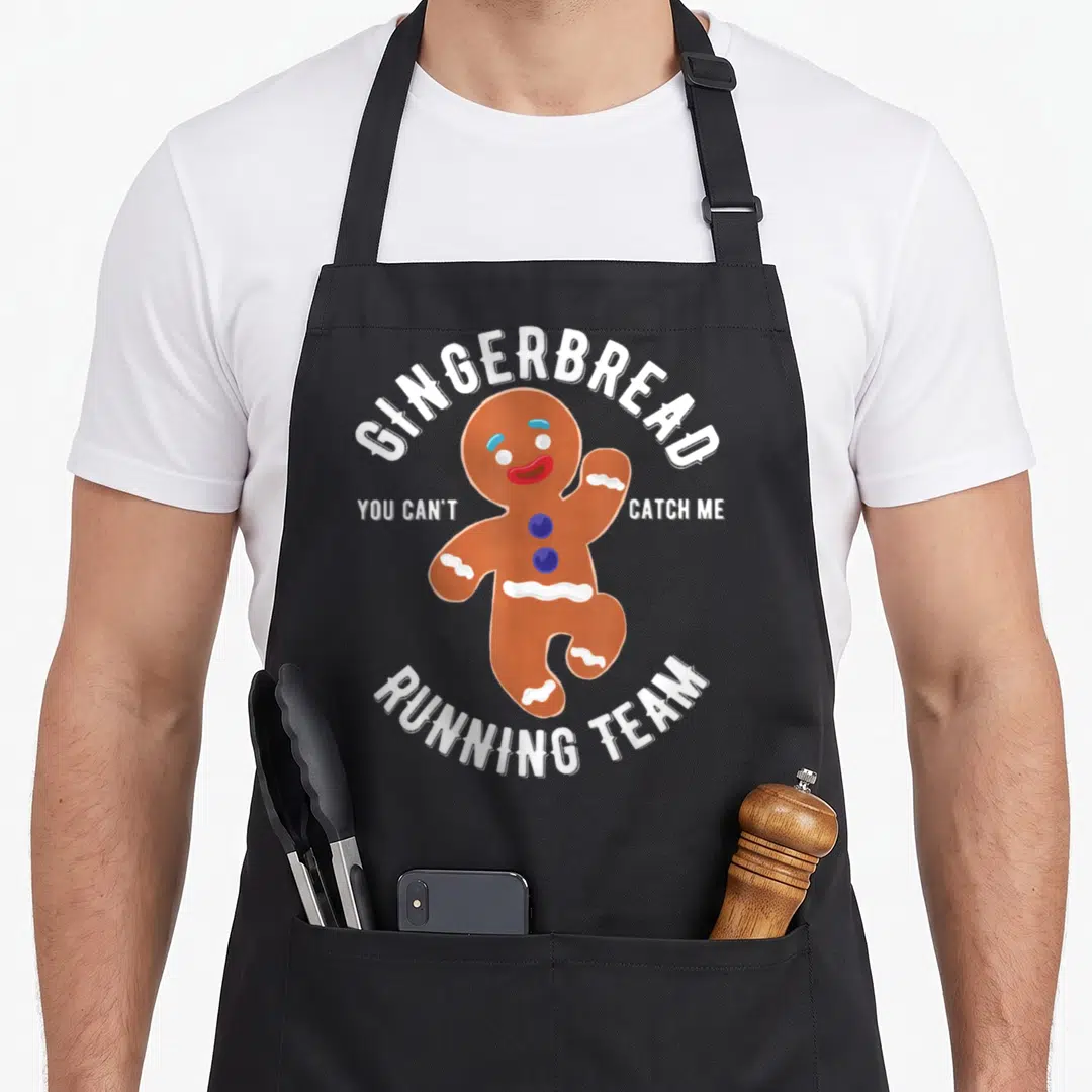 Running christmas gingerbread apron - Cartoon gingerbread man running with GINGERBREAD RUNNING TEAM text in brown — shown on a black cotton canvas apron against a white background