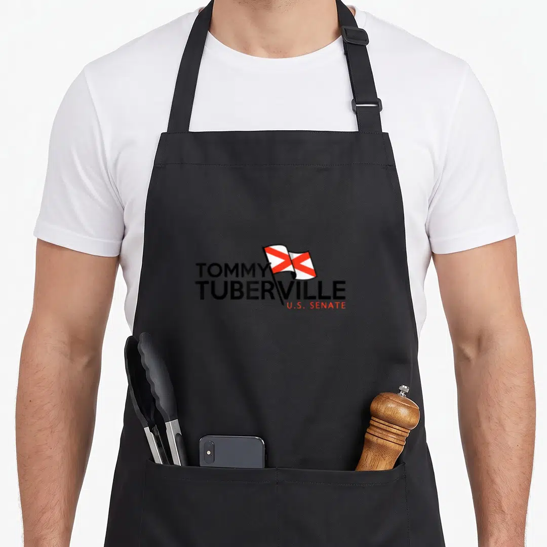Tommy alabama apron - TOMMY TUBERVILLE U.S. SENATE text with red and white flag graphic — shown on a black cotton canvas apron against a white background