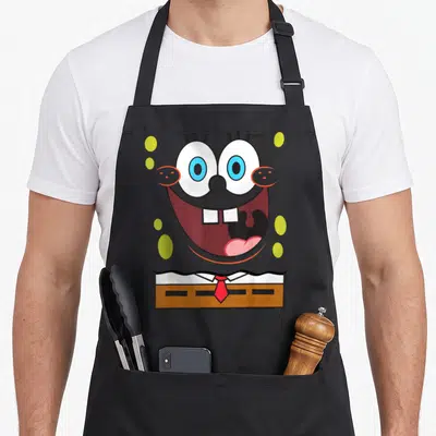 Funny squarepant character aprons - SpongeBob face with open mouth, red tie, yellow-green circles — shown on a black cotton canvas apron against a white background