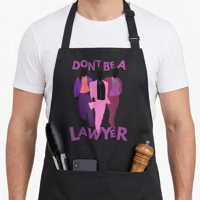 Girlfriend modern apron - DON'T BE A LAWYER text above three men in purple pink and black suits — shown on a black cotton canvas apron against a white background