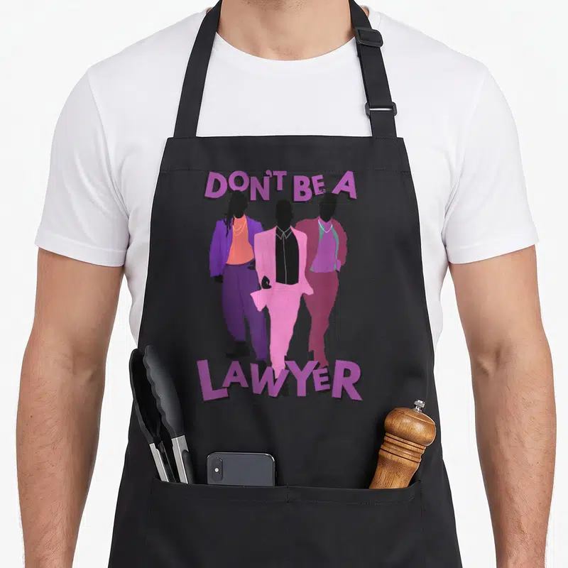 Girlfriend modern apron - DON'T BE A LAWYER text above three men in purple pink and black suits — shown on a black cotton canvas apron against a white background