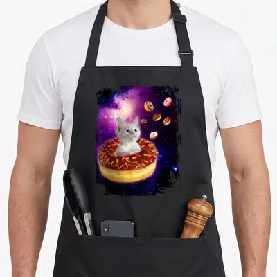 Cat donut apron - White cat in chocolate frosted donut floating in purple blue galaxy with distressed black border — shown on a black cotton canvas apron against a white background
