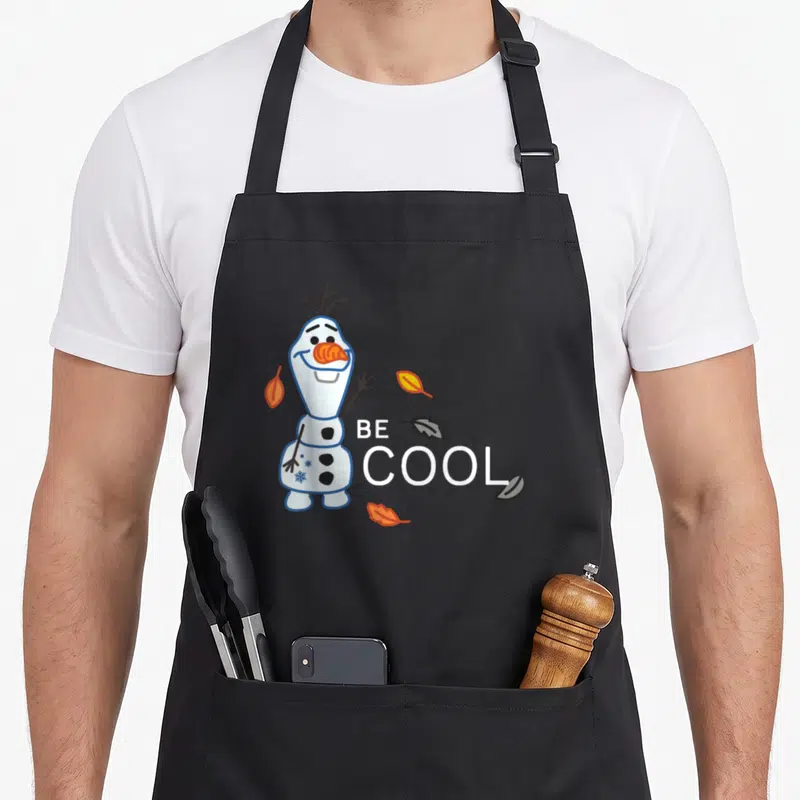Funny olaf frozen apron - Cartoon snowman stands beside stacked BE COOL text with scattered autumn leaves in blue — shown on a black cotton canvas apron against a white background