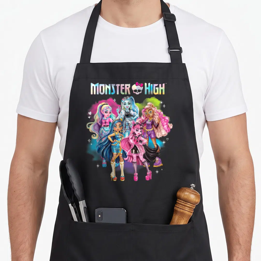 Monster rainbow apron - Five cartoon Monster High characters under a rainbow skull logo with pink, blue, purple — shown on a black cotton canvas apron against a white background