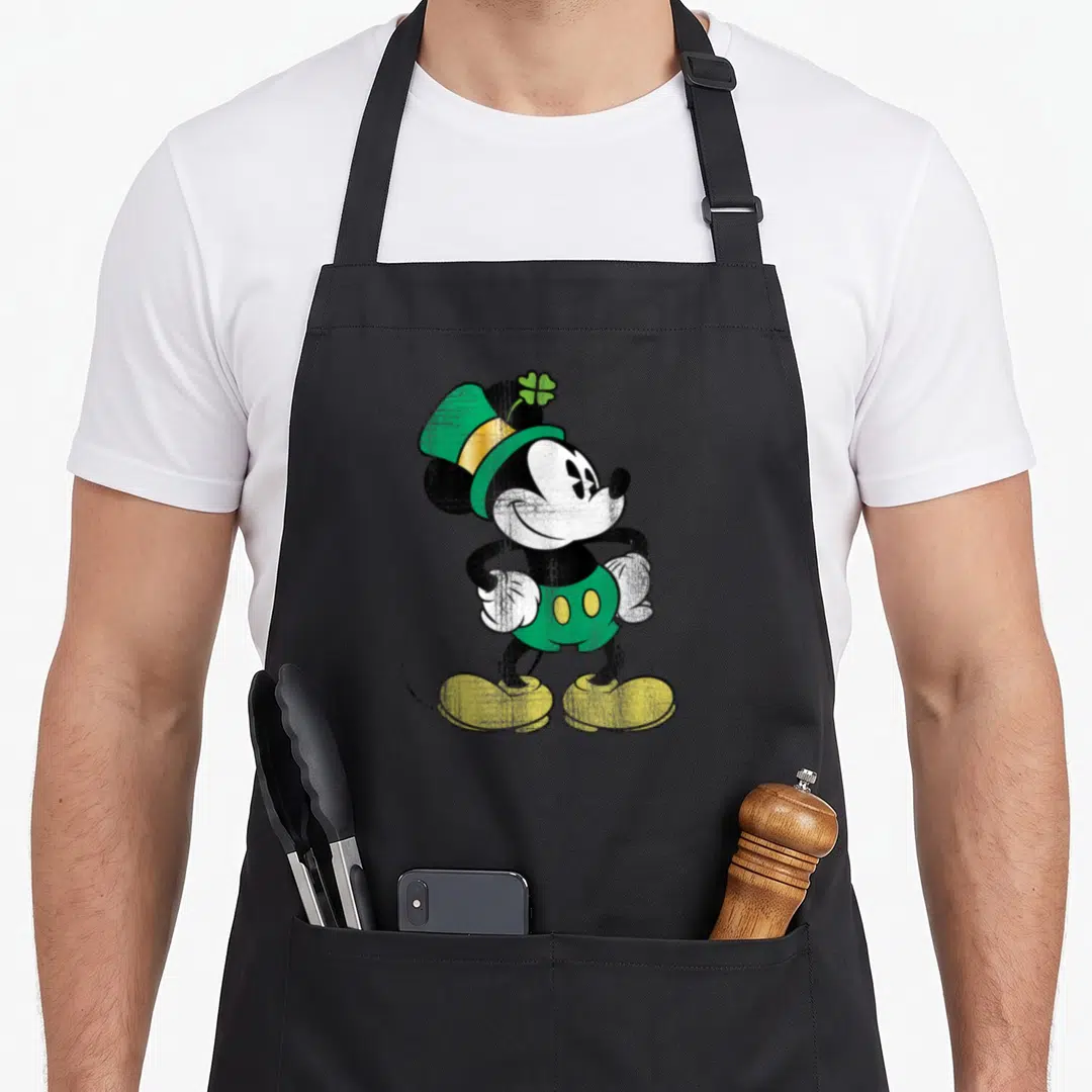 Cute leprechaun st patrick day aprons - Mickey Mouse cartoon wearing green leprechaun hat with shamrock and green — shown on a black cotton canvas apron against a white background