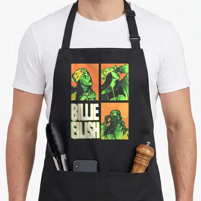 Billie square apron - Retro four-panel print with Billie Eilish portraits and white BILLIE EILISH text in orange green — shown on a black cotton canvas apron against a white background