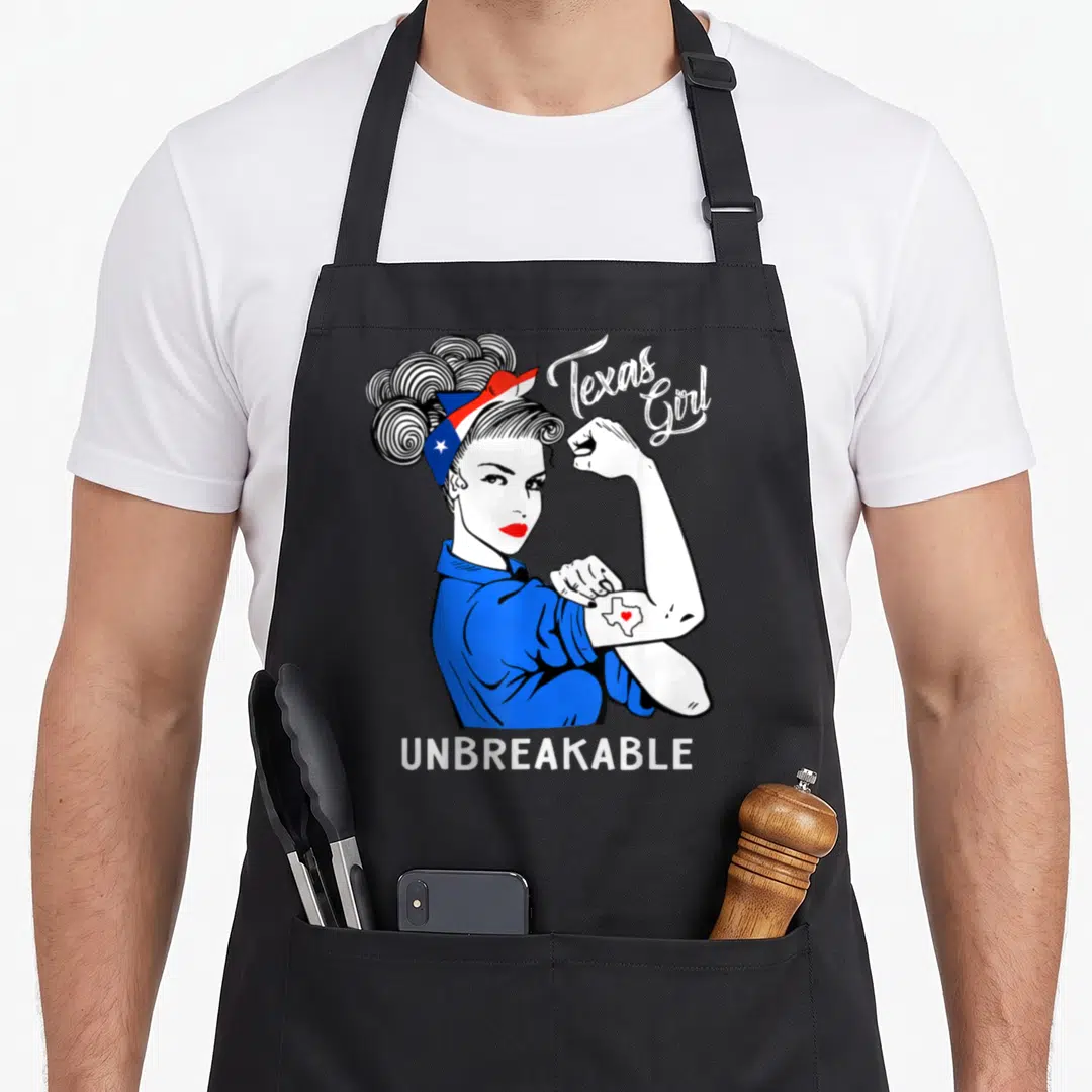 Unbreakable texas apron - Woman flexing arm with Texas map tattoo and UNBREAKABLE text in blue white red black — shown on a black cotton canvas apron against a white background