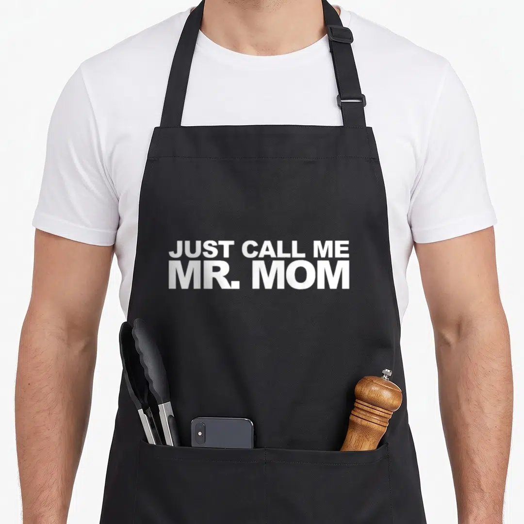 Call mr mom apron - White text reading JUST CALL ME MR. MOM stacked in two lines — shown on a black cotton canvas apron against a white background