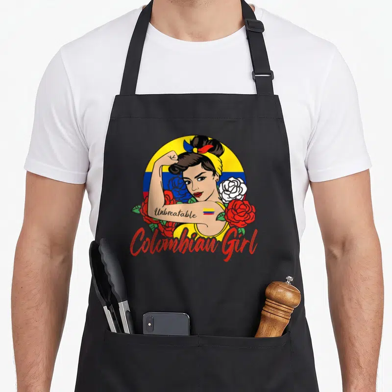 Mujer colombia apron - Cartoon woman flexing arm with Unbreakable text and Colombian flag roses on circular background — shown on a black cotton canvas apron against a white background