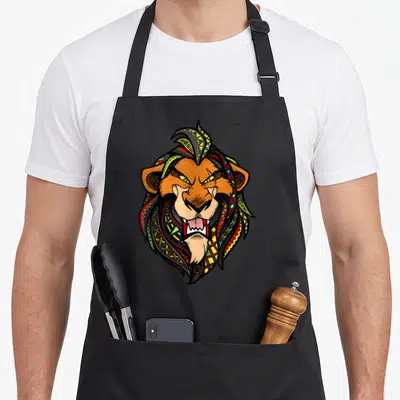 Pattern lion apron - Line-art lion head filled with orange, yellow, red, green, and black tribal geometric patterns — shown on a black cotton canvas apron against a white background