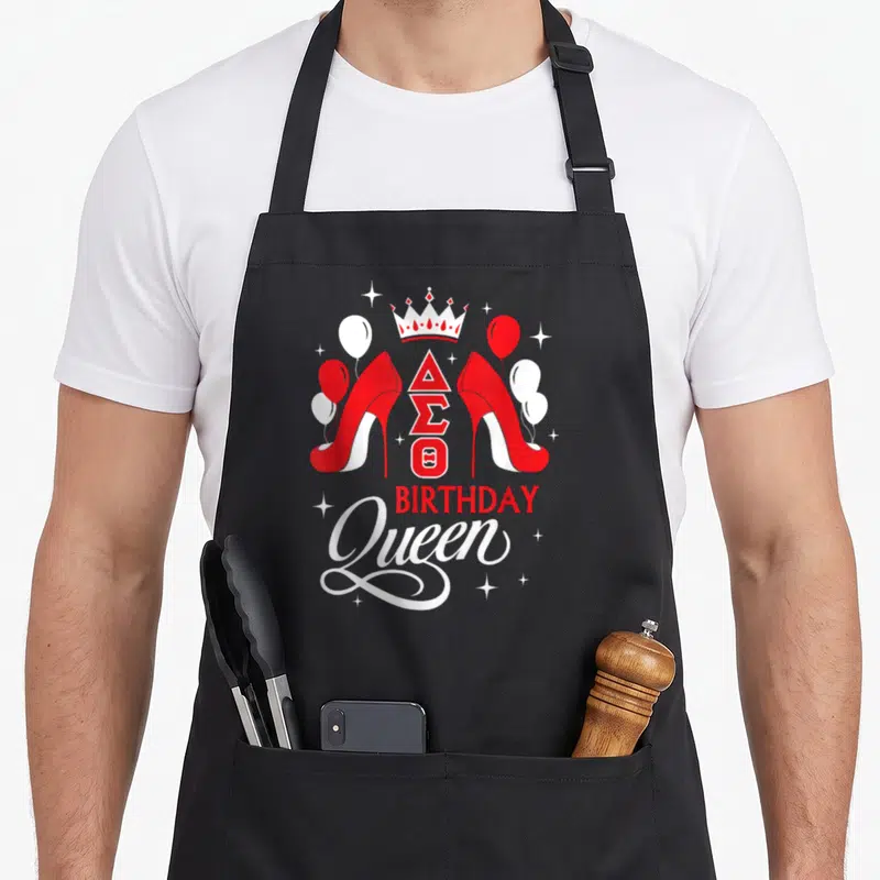 Sigma birthday apron - Red high heels flanking Delta Sigma Theta letters under crown with Birthday Queen text — shown on a black cotton canvas apron against a white background