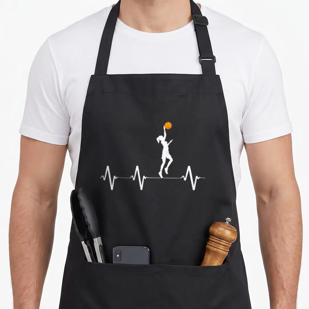 Funny heartbeat basketball apron - White silhouette of a player jumping to shoot an orange ball above a white heartbeat — shown on a black cotton canvas apron against a white background