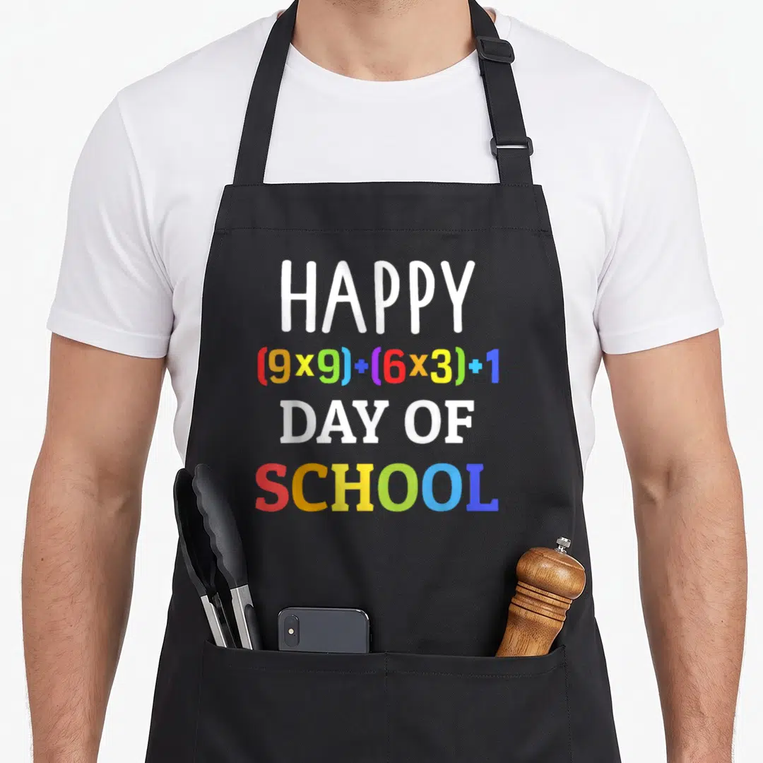 100th formula apron - Stacked text reading HAPPY 9x9 plus 6x3 plus 1 DAY OF SCHOOL in rainbow colors — shown on a black cotton canvas apron against a white background