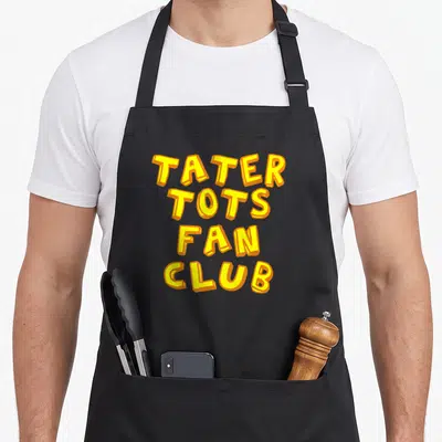 Tater apron or apron - Yellow and orange TATER TOTS FAN CLUB stacked block lettering on black background — shown on a black cotton canvas apron against a white background