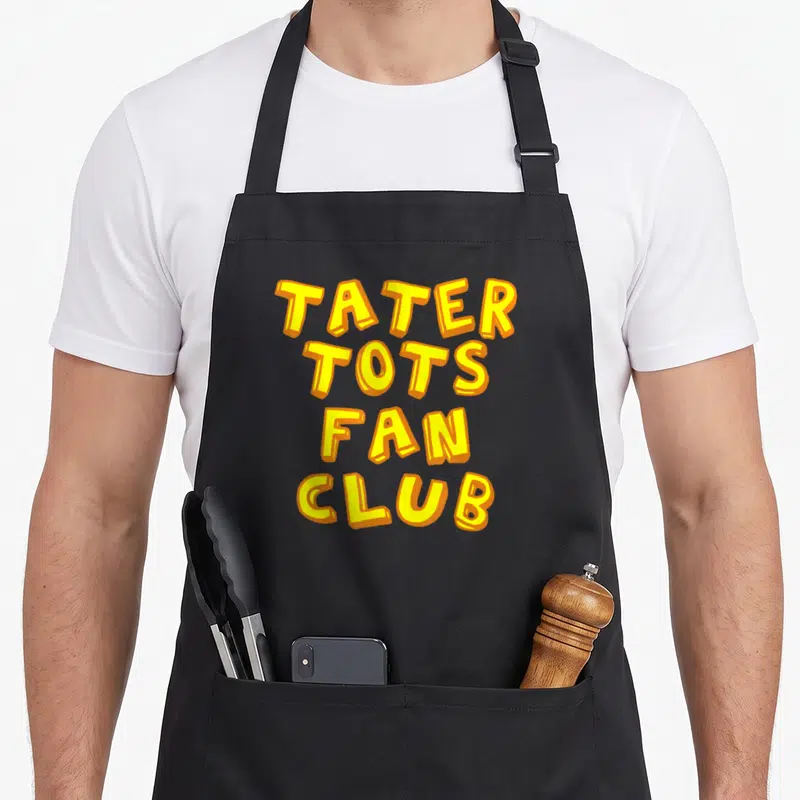 Tater apron or apron - Yellow and orange TATER TOTS FAN CLUB stacked block lettering on black background — shown on a black cotton canvas apron against a white background