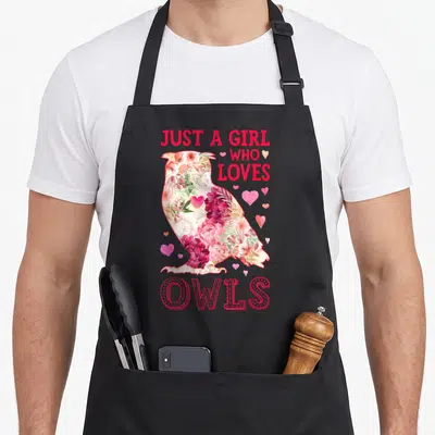 Owl flower the floral apron - Floral owl silhouette filled with red pink white flowers and hearts with text Just A Girl — shown on a black cotton canvas apron against a white background