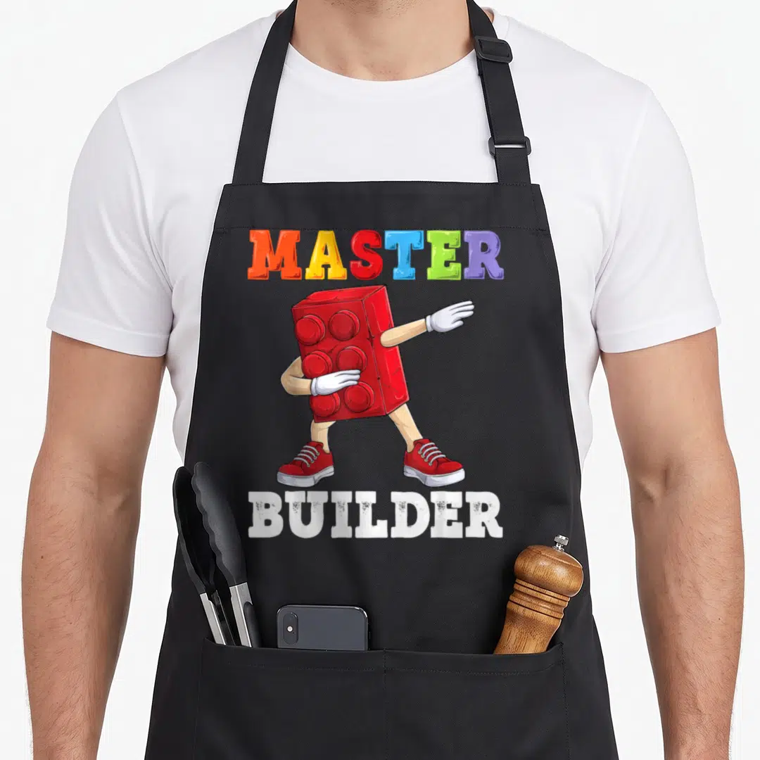 Dabbing building apron - Red toy brick character dabbing under colorful MASTER BUILDER text — shown on a black cotton canvas apron against a white background