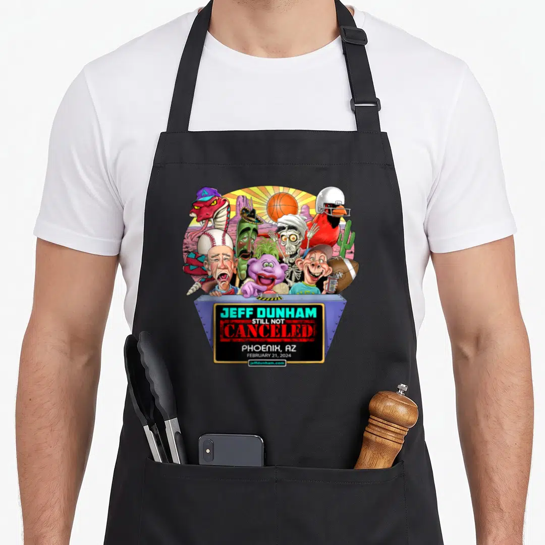 Phoenix hollywood apron - Jeff Dunham puppets behind podium with Still Not Canceled text and Phoenix AZ date — shown on a black cotton canvas apron against a white background