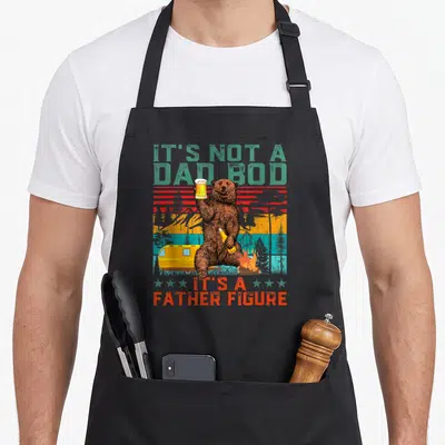 Bear father day apron - Brown bear holding beer mug and bottle near camper and campfire with retro striped background — shown on a black cotton canvas apron against a white background