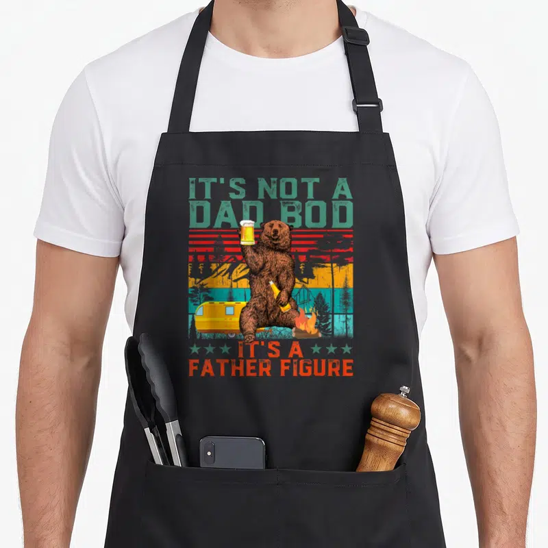 Bear father day apron - Brown bear holding beer mug and bottle near camper and campfire with retro striped background — shown on a black cotton canvas apron against a white background