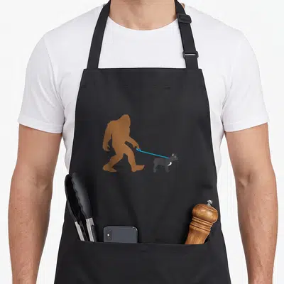 Bigfoot french bulldog apron - Brown Bigfoot silhouette walking a small grey cat on a blue leash — shown on a black cotton canvas apron against a white background