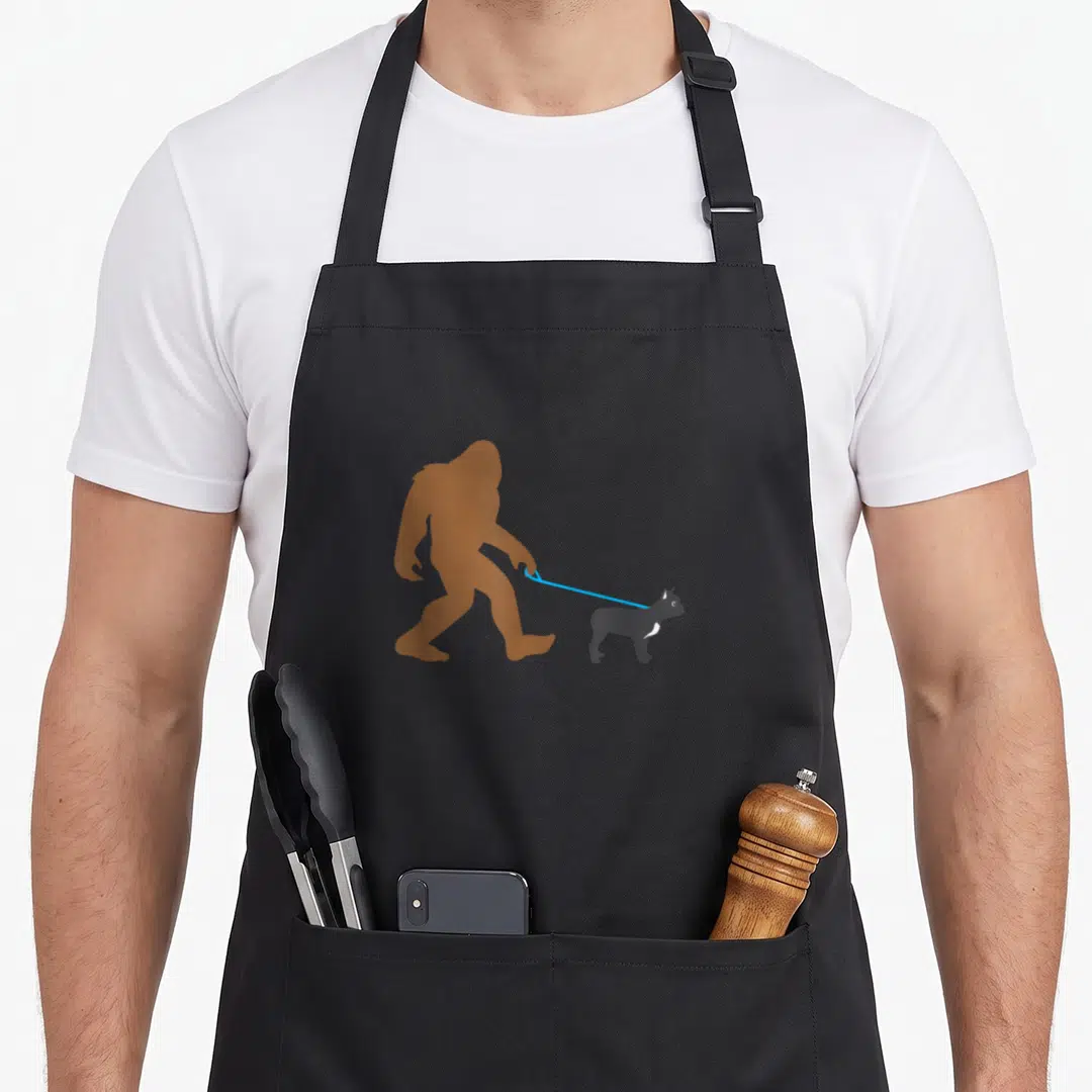 Bigfoot french bulldog apron - Brown Bigfoot silhouette walking a small grey cat on a blue leash — shown on a black cotton canvas apron against a white background
