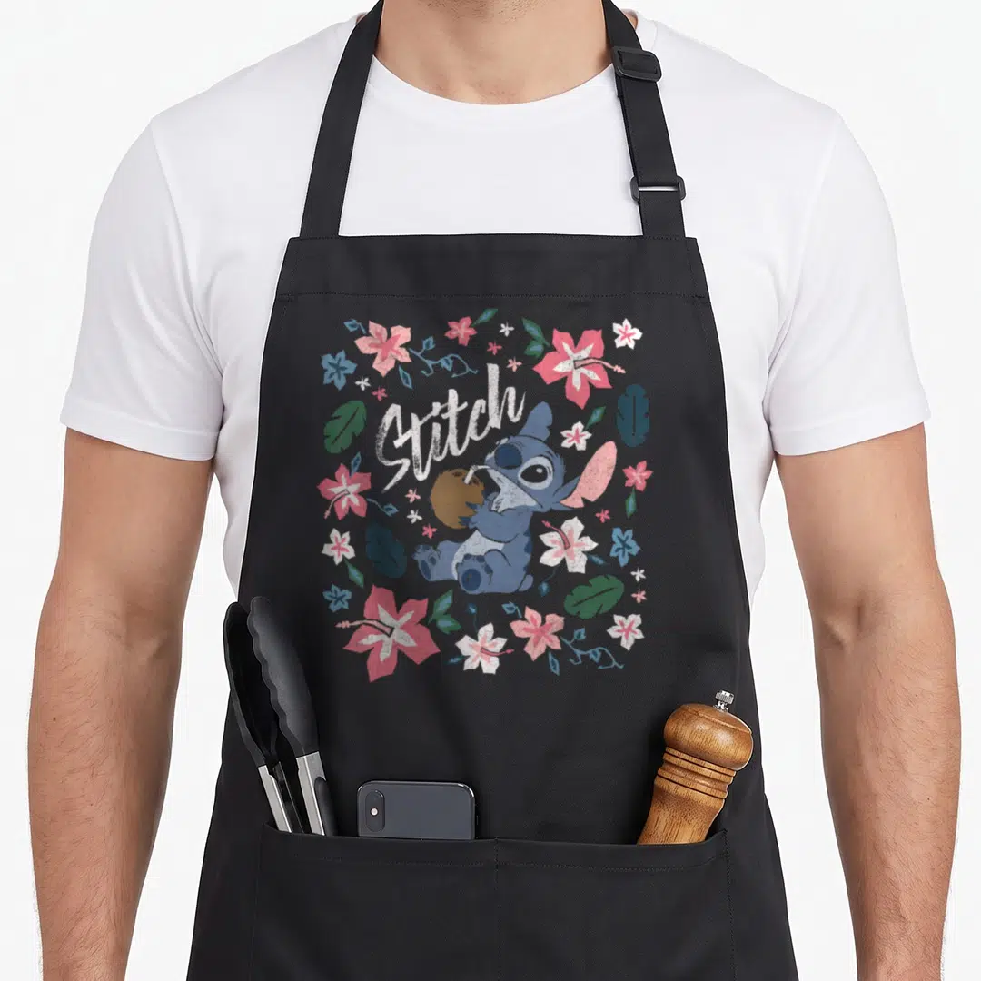 Stitch floral apron - Blue cartoon character holding coconut with straw surrounded by pink and white tropical flowers — shown on a black cotton canvas apron against a white background