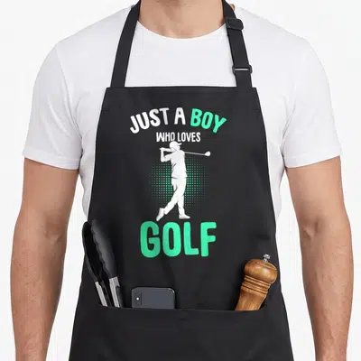 Cute golfer golf apron - White golfer silhouette over mint green halftone dots with Just a Boy Who Loves Golf text — shown on a black cotton canvas apron against a white background
